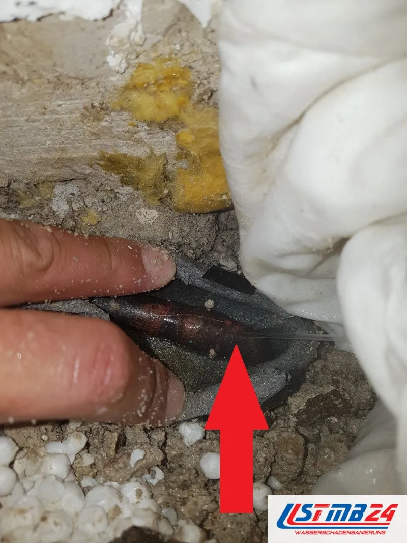Leckortung in Geesthacht: Finger halten die graue Rohrdämmung zur Seite, ein roter Pfeil zeigt auf die Schadstelle am Kupferrohr
