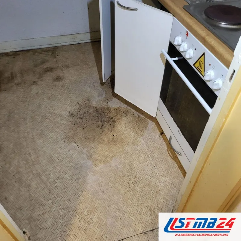 Wasserschaden Notdienst in Geesthacht: Teeküche mit dunklen Wasserflecken auf dem Boden vor Herd und Spülenschrank