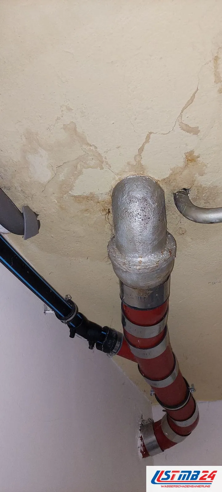 Rohrbruch in Geesthacht: Gussbogen an der Decke, darunter ein rot-silbern umwickeltes Abflussrohr, an der Decke Wasserränder