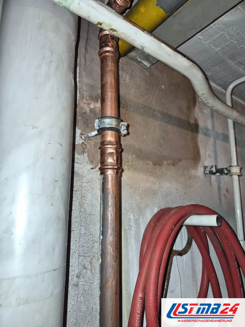 Sanitär und Heizung in Geesthacht: senkrechtes Kupferrohr mit Rohrschelle an der Wand, daneben ein aufgerollter roter Schlauch