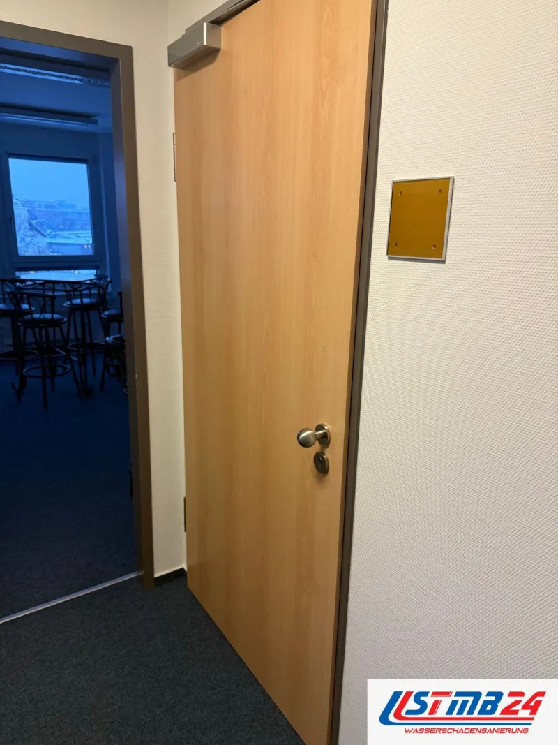 Tischler in Geesthacht: Bürotür in Buche mit Obentürschließer und Türschild, dahinter ein Raum mit Stehtischen