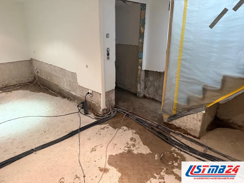 Wasserschaden in Grömitz: Souterrain mit abgeschlagenem Sockelputz, Kabel auf fleckigem Estrich, die Treppe mit Folie abgeklebt