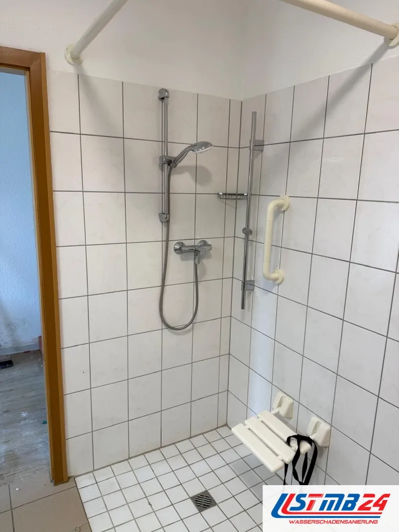 Badsanierung in Grömitz: bodengleiche Dusche mit weißen Wandfliesen, Brausestange, Haltegriff, Klappsitz und Vorhangstange