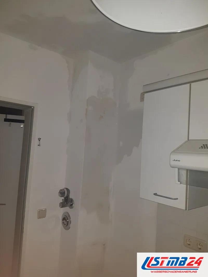 Badsanierung in Grömitz: Bad nach dem Fliesenrückbau, Wand mit dunklen Wasserflecken, Armaturenanschlüsse und ein Hängeschrank