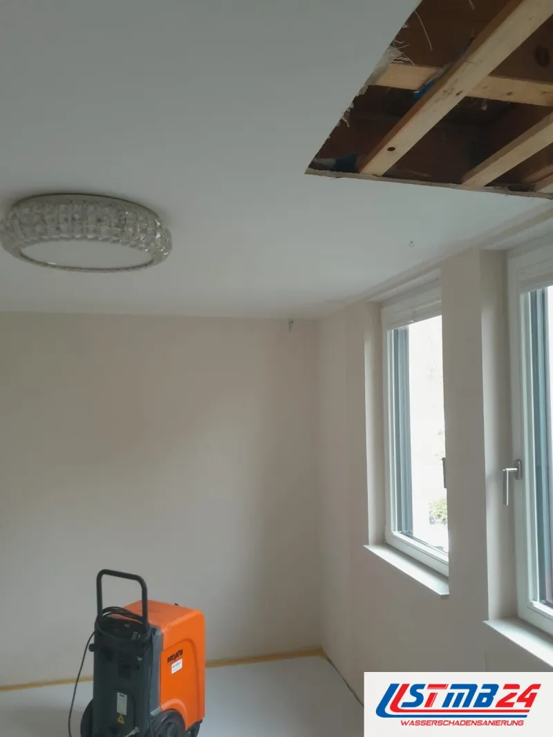 Bautrocknung in Grömitz: orangefarbener Trockner in einem leeren Zimmer, in der Decke ist ein Feld bis auf die Lattung geöffnet