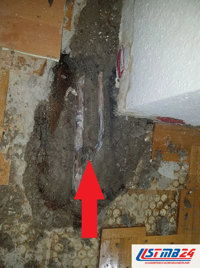 Leckortung in Grömitz: Mosaikparkett aufgenommen, Estrich geöffnet, ein roter Pfeil zeigt auf die Schadstelle am Kupferrohr