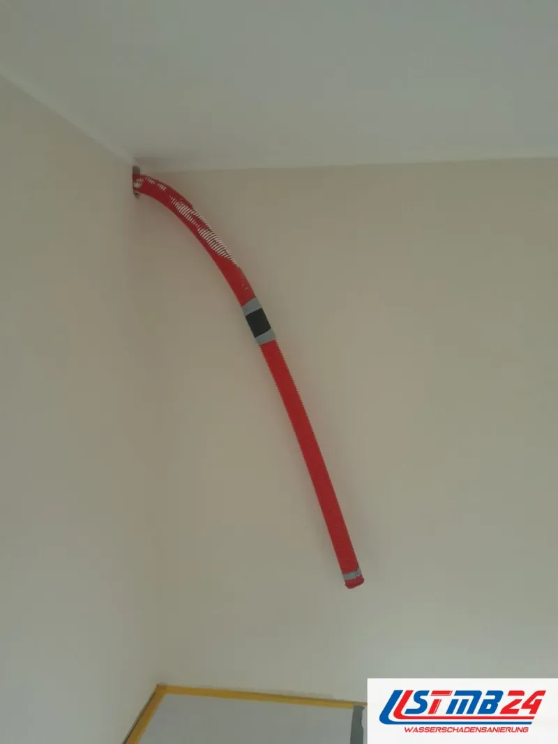 Maler in Grömitz: frisch gestrichene Wand, unten Vlies mit gelbem Klebeband, oben ein roter Schlauch an der Wand