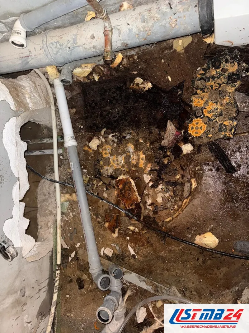 Wasserschaden Notdienst in Grömitz: aufgestemmter Boden unter grauen Abflussrohren, nasser Untergrund mit Resten von altem Belag