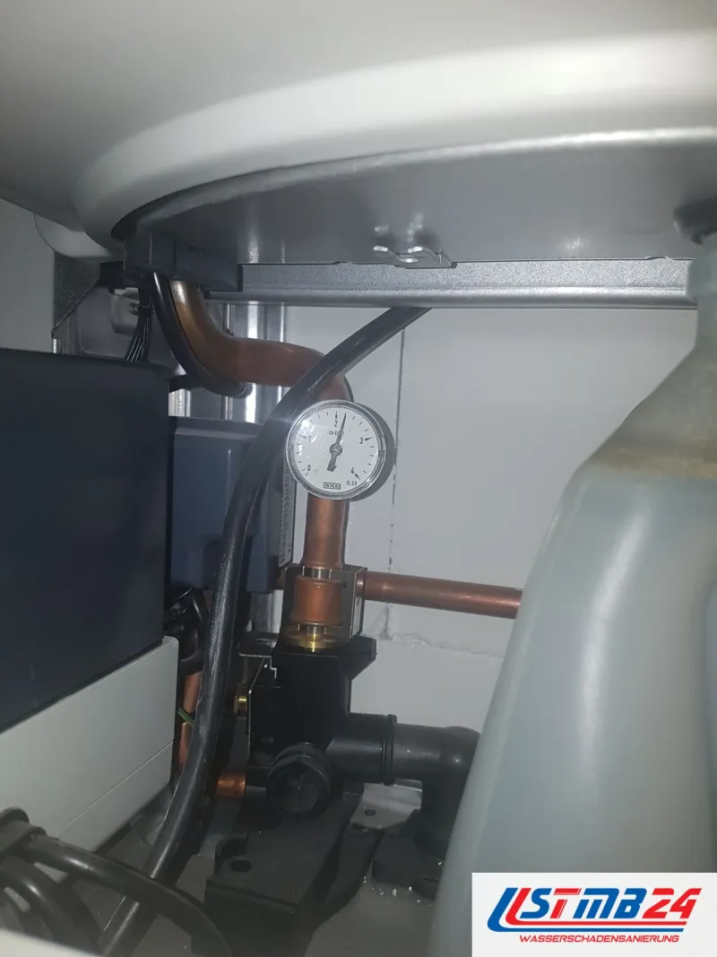 Sanitär und Heizung in Grömitz: Unterseite eines Speichers mit Kupferanschluss, Manometer und Pumpe, rechts ein Kanister