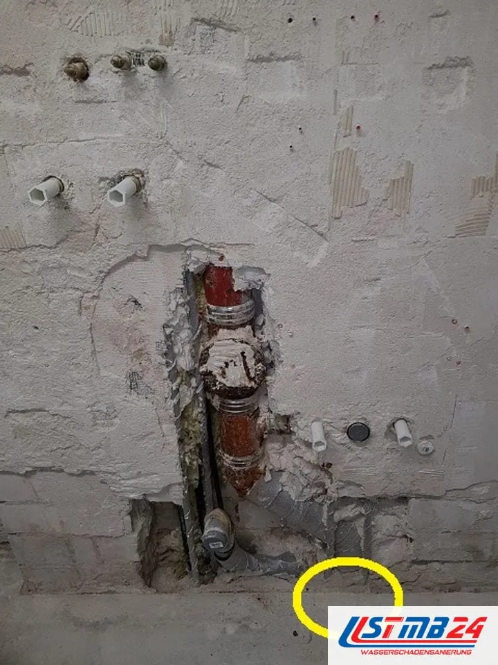 Sanitär und Heizung in Grömitz: aufgestemmte Wand mit rostigem Gussabfluss, Anschlüssen und gelb eingekreister Stelle am Boden