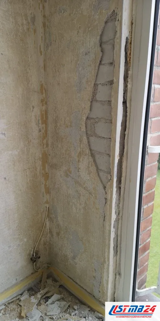 Schimmelsanierung in Grömitz: Fensterlaibung mit abgelöstem Putz bis aufs Mauerwerk, die Wand fleckig, unten Schutt