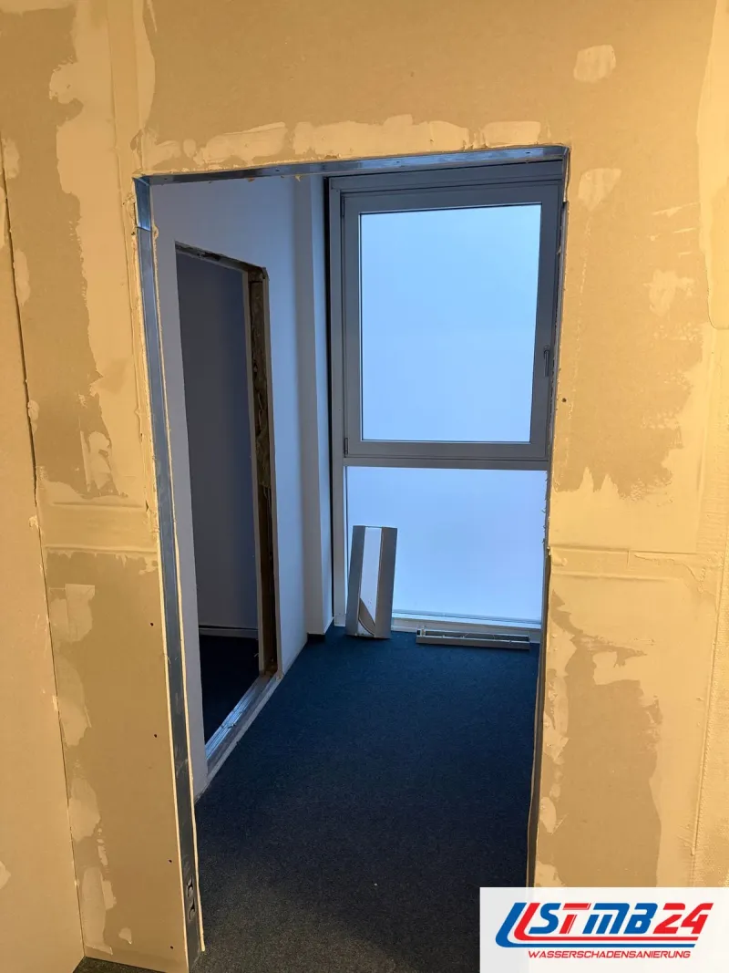 Trockenbauarbeiten im Büro: neue Wand mit Türöffnung, Fugen und Schrauben gespachtelt, dahinter blauer Teppich