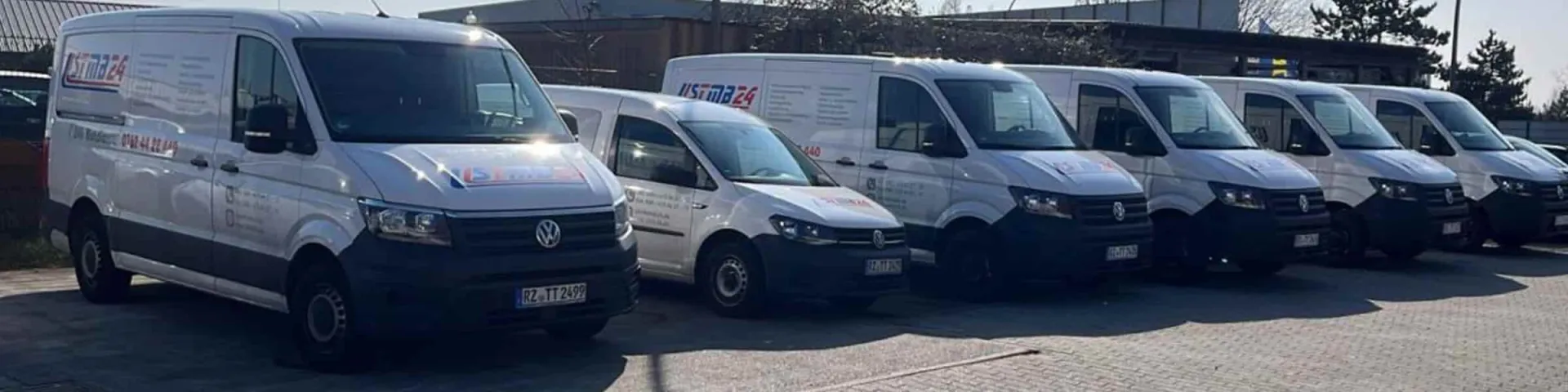 Über uns: weiße Transporter der STMB24 mit Firmenbeschriftung, nebeneinander geparkt
