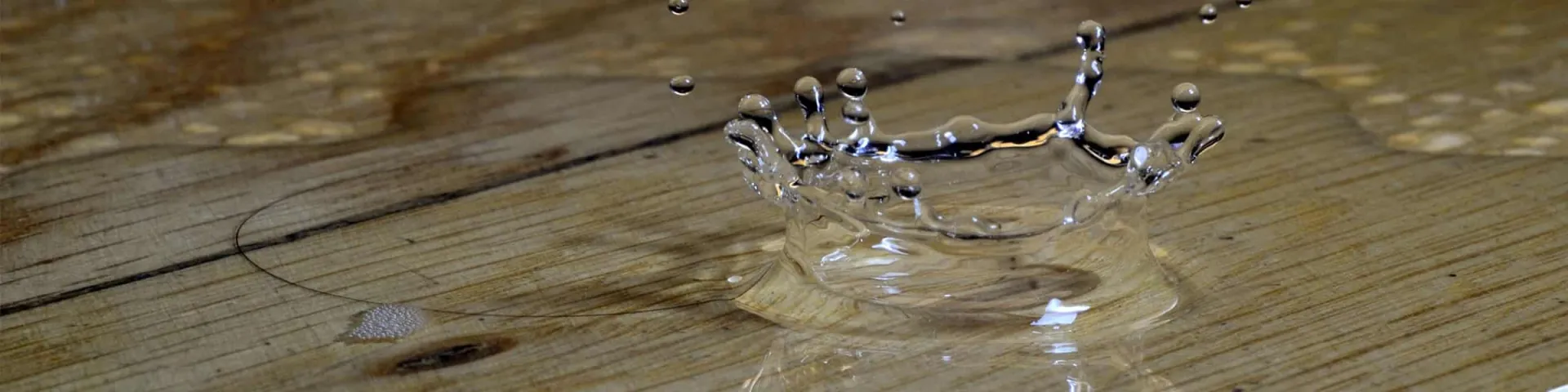 Wasserschadensanierung: Wassertropfen schlägt auf einem nassen Holzboden auf