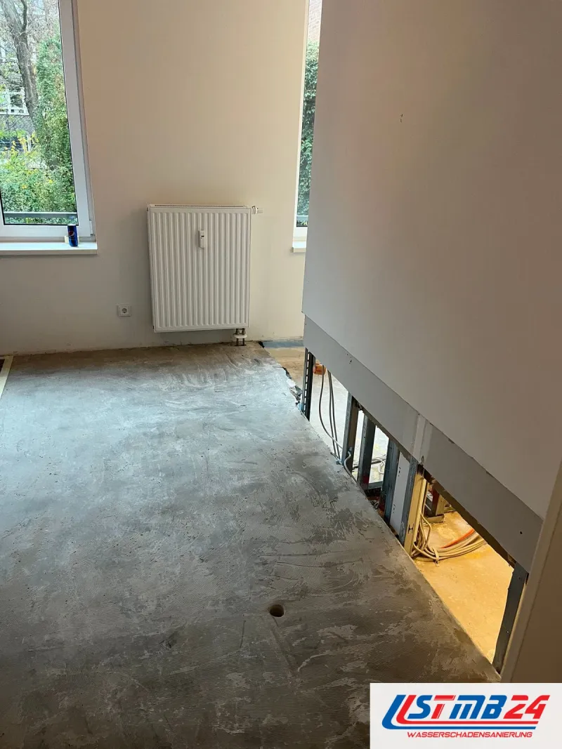 Wohnraum ohne Bodenbelag, die Trockenbauwand unten geöffnet, dahinter Ständerwerk und Leitungen